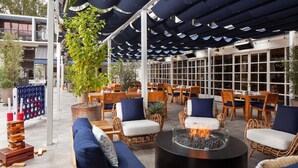 An outdoor seating area with wicker chairs and sofas, a central fire pit, and a row of windows. - Sheraton Universal Hotel (Universal City)