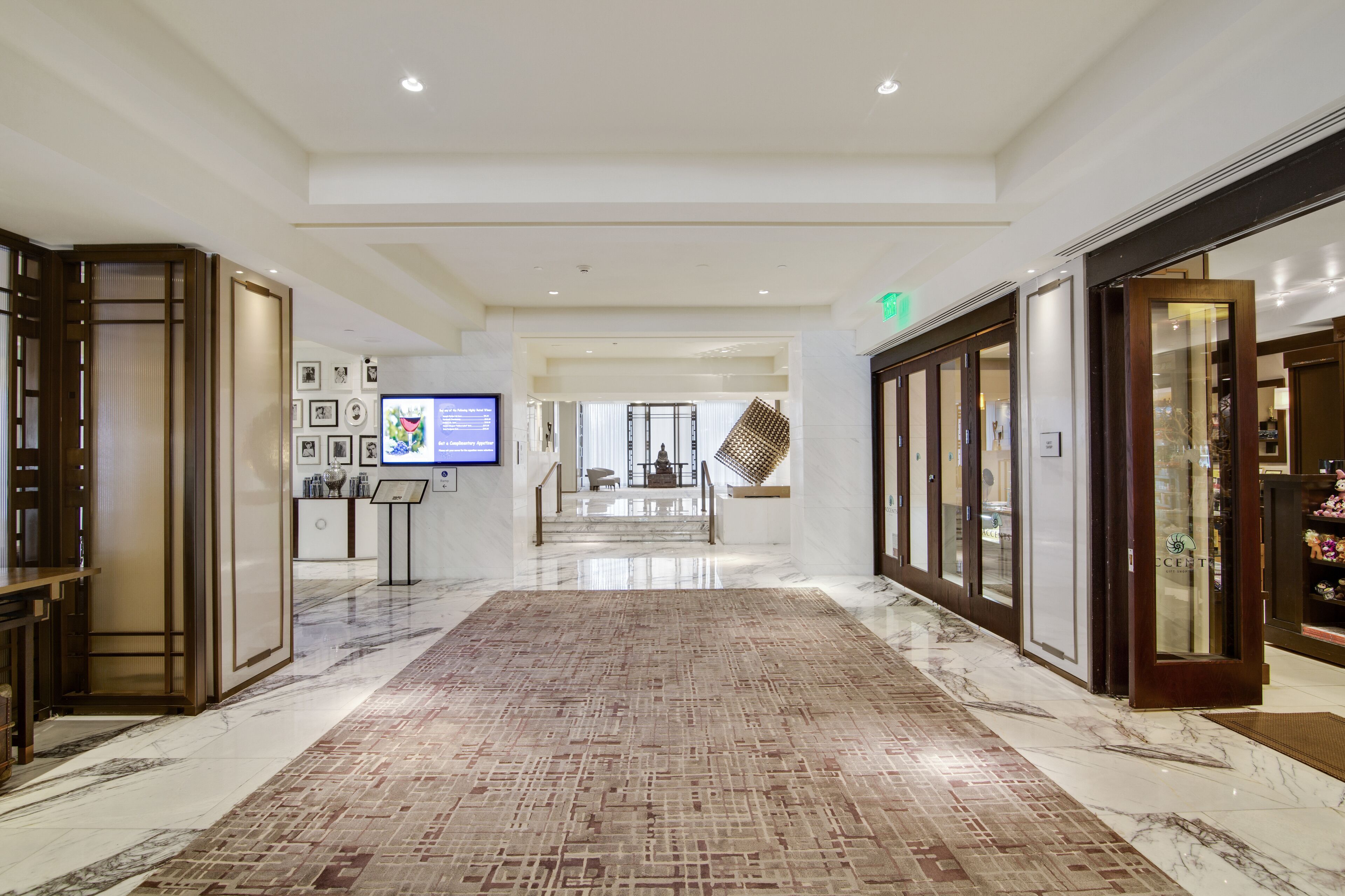 A spacious hotel lobby with a marble floor, a reception desk, a digital display, and a view into the dining area.