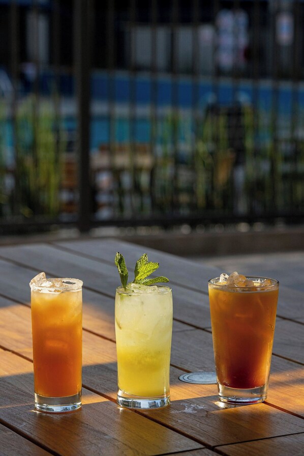 Tres vasos de bebidas heladas sobre una mesa de madera al aire libre.