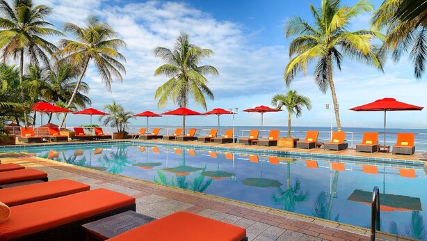 A poolside area with lounge chairs and umbrellas, palm trees, and a view of the ocean. - Hotel Re-Ndama (Libreville)