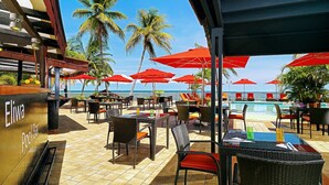 An outdoor seating area with red umbrellas, wicker furniture, and a pool view. - Hotel Re-Ndama (Libreville)
