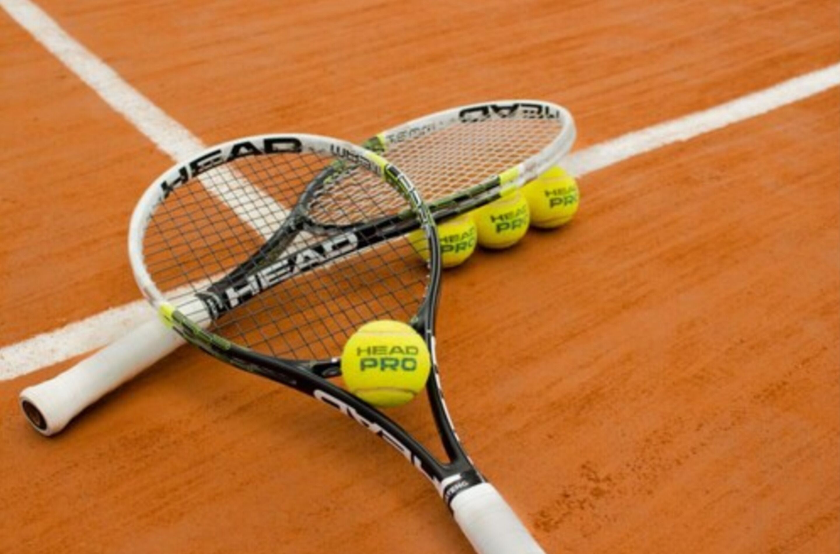 Two tennis rackets and three tennis balls on a clay court.