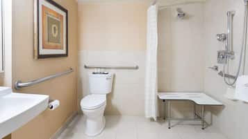 A bathroom with a toilet, sink, shower, and a small table.