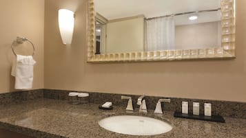 A bathroom with a granite countertop, a white sink, a mirror, and a towel rack.