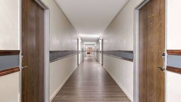 Un largo y estrecho pasillo de hotel con puertas de madera a ambos lados, suelo de color claro e iluminación empotrada en el techo.