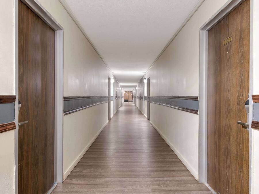 Un largo y estrecho pasillo de hotel con puertas de madera a ambos lados, suelo de color claro e iluminación empotrada en el techo.