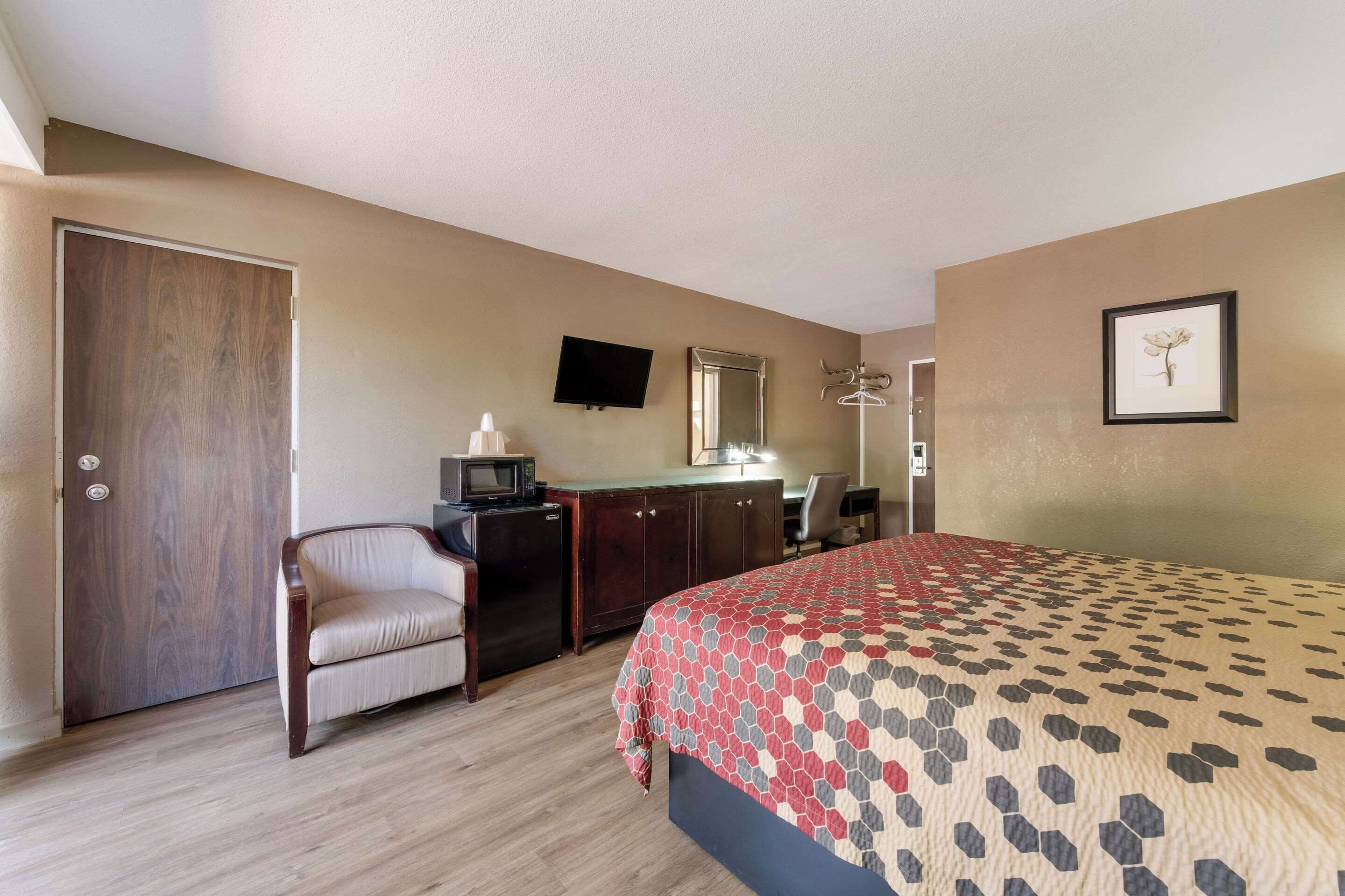 A hotel room with a bed, a desk with a computer, a chair, a wardrobe, a television, and a framed picture on the wall.