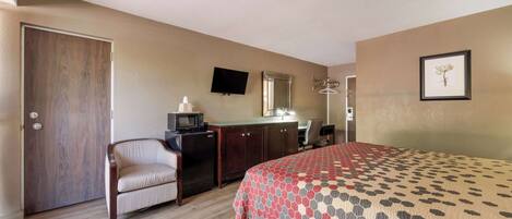 A hotel room with a bed, a desk with a computer, a chair, a wardrobe, a television, and a framed picture on the wall.