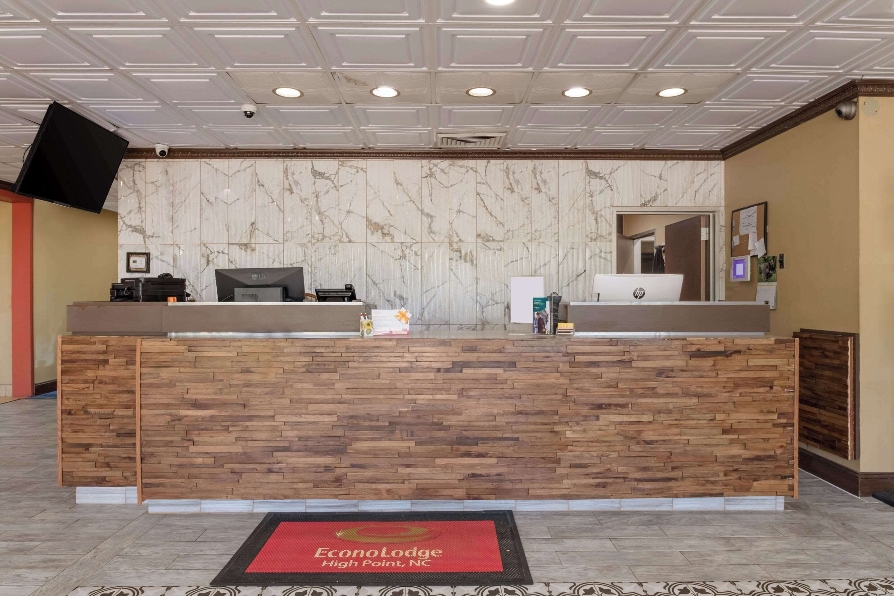 Un comptoir d’accueil avec un mur en marbre, un comptoir en bois et un paillasson rouge.