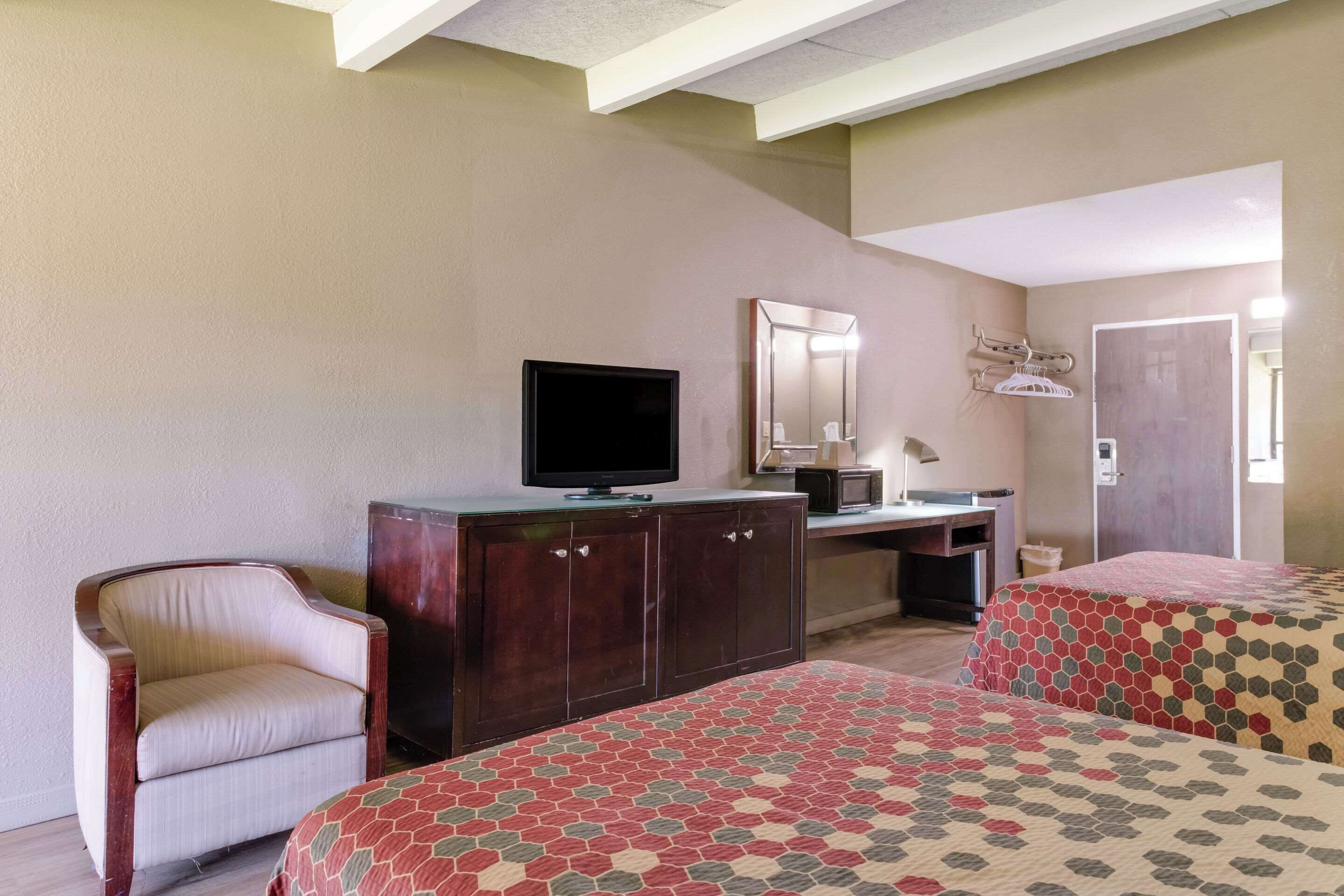 A hotel room with two beds, a desk, a chair, a television, and a mirror.