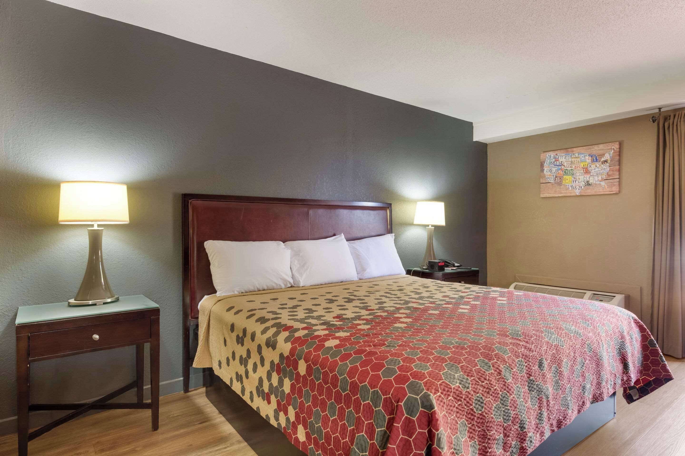 A hotel room with a large bed, two bedside tables with lamps, a wall map, and a window with curtains.