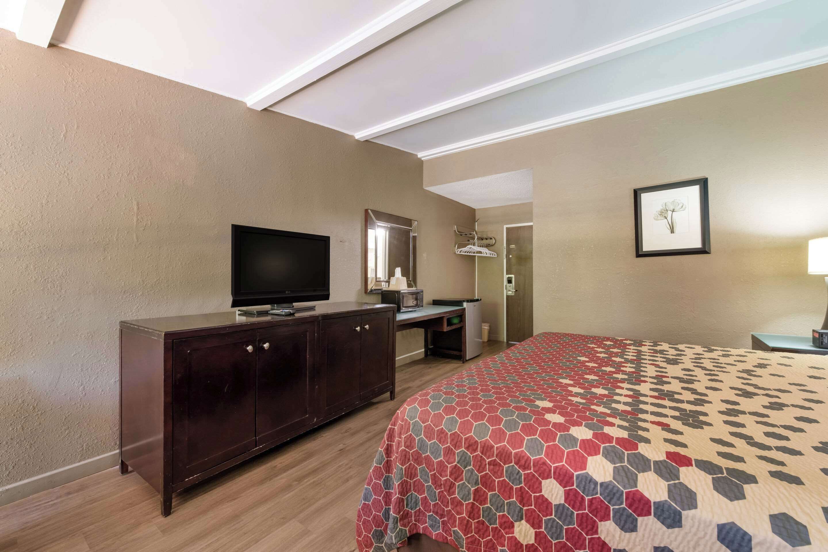 A hotel room with a bed, a TV, a dresser, a desk, a mirror, and a framed picture on the wall.