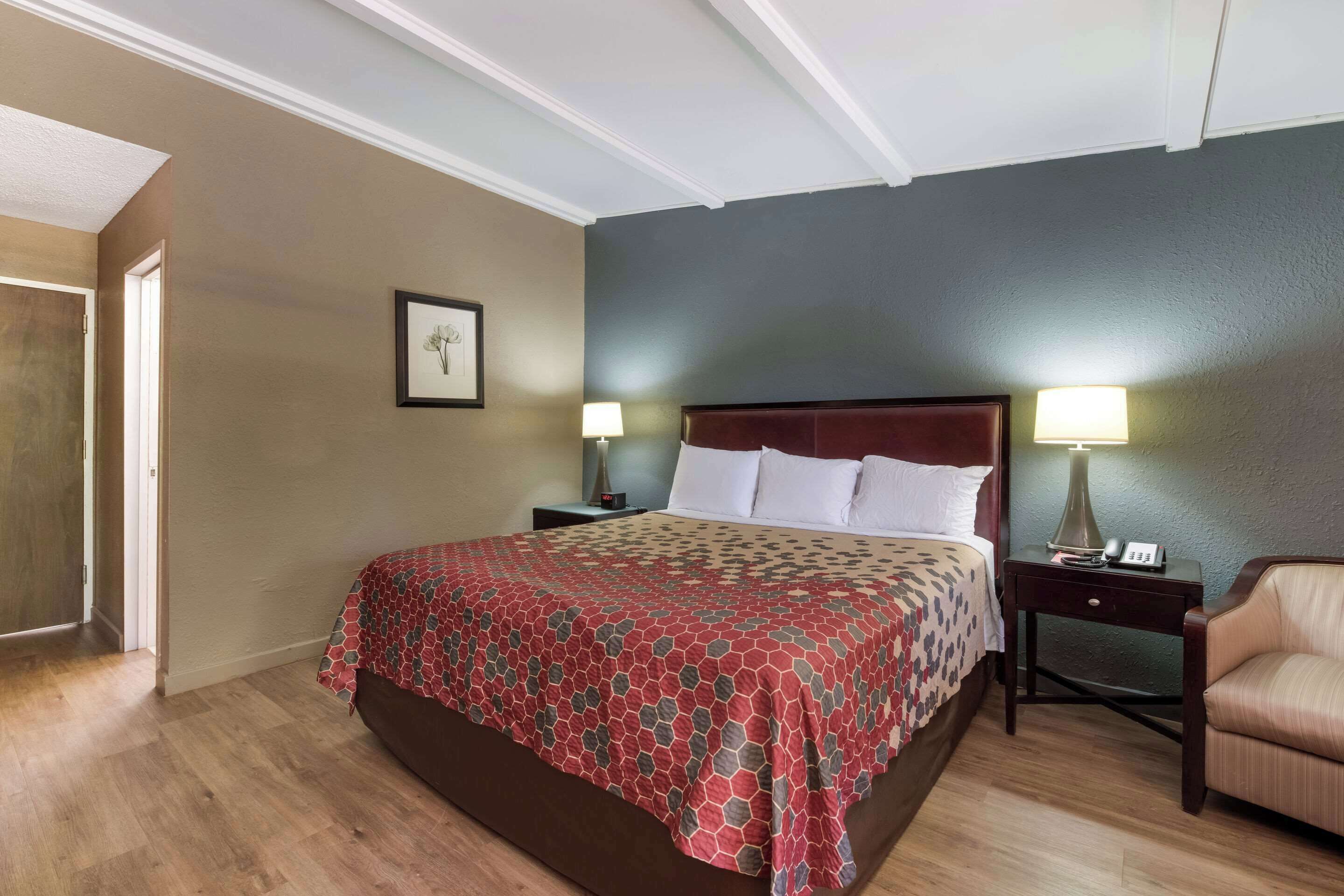 Habitación de hotel con una cama grande, dos mesitas de noche con lámparas, una silla y un cuadro enmarcado en la pared.
