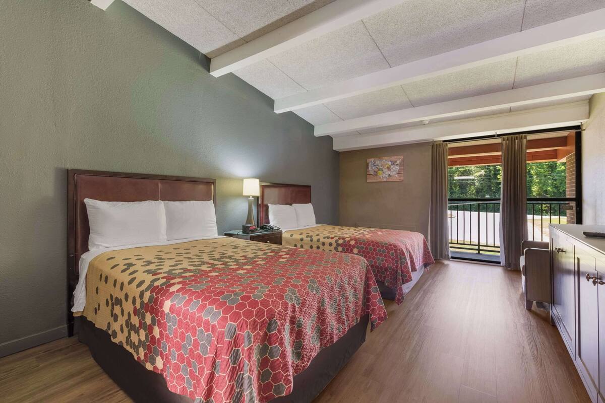 A hotel room with two beds, a desk, and a view of the outdoors.