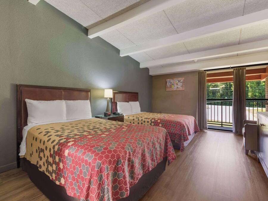A hotel room with two beds, a desk, and a view of the outdoors.