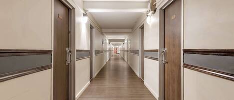 A long, narrow hotel corridor with wooden floors and doors on both sides.