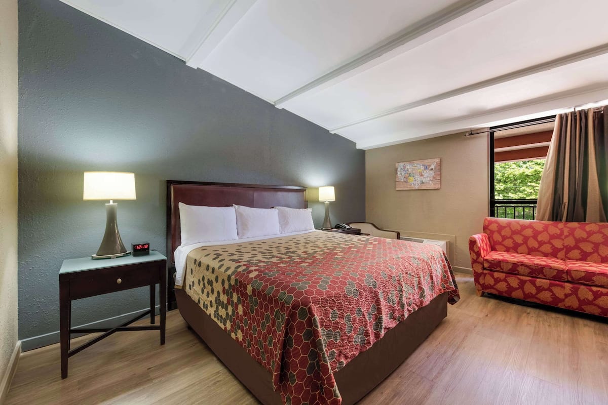 A hotel room with a bed, two bedside tables with lamps, a red patterned sofa, a window with curtains, and a map on the wall.