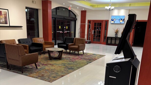 A modern lobby with leather sofas, a coffee table, a piano, and a TV on the wall.