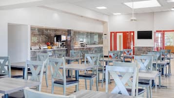A cafeteria with multiple tables and chairs, a coffee machine, and a counter with food items.