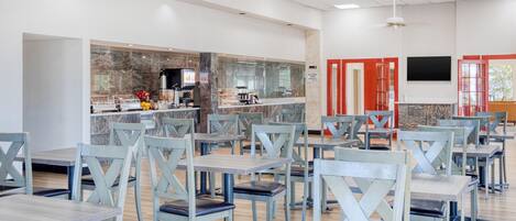 A cafeteria with multiple tables and chairs, a coffee machine, and a counter with food items.