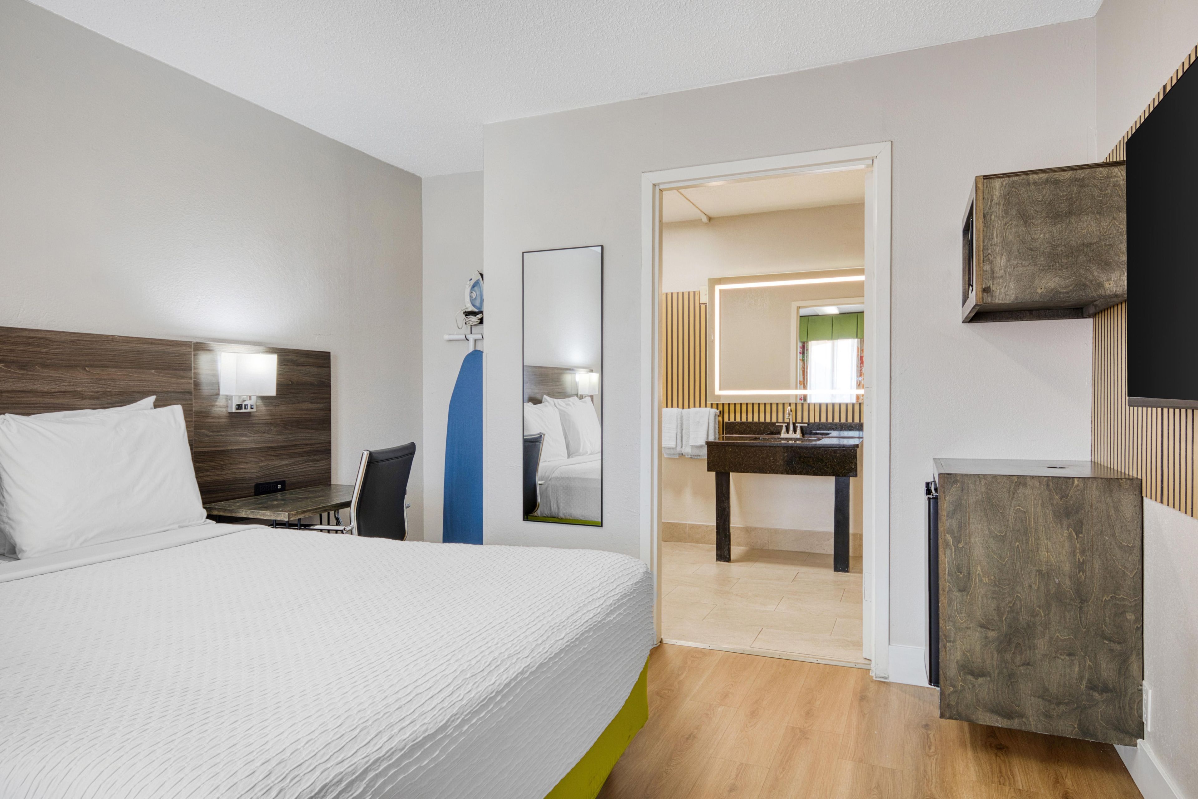 A hotel room with a large bed, a desk, a mirror, and a bathroom visible through an open door.