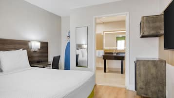A hotel room with a large bed, a desk, a mirror, and a bathroom visible through an open door.