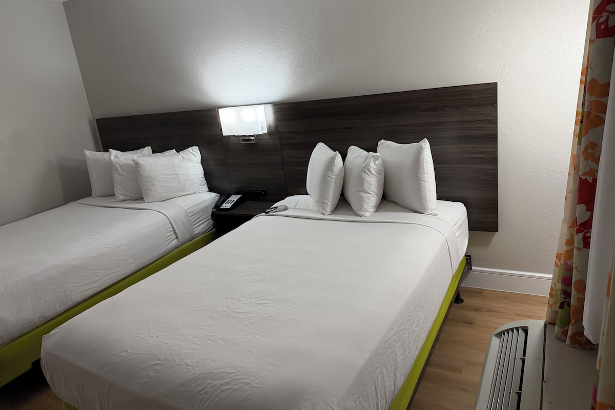 A hotel room with two beds, a bedside telephone, and a window with curtains.