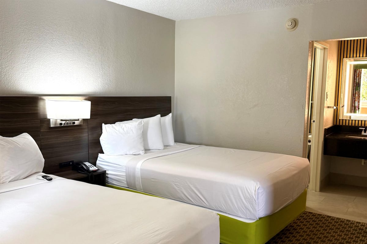 Two single beds with white linens, a bedside phone, a wall-mounted lamp, and a bathroom visible through an open door.