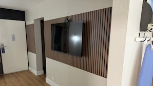 A hotel room with a flat-screen TV mounted on a wall with vertical wooden paneling, a wooden floor, and a door with a sign.