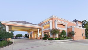 A hotel entrance with a covered driveway, multiple columns, and a parking lot.