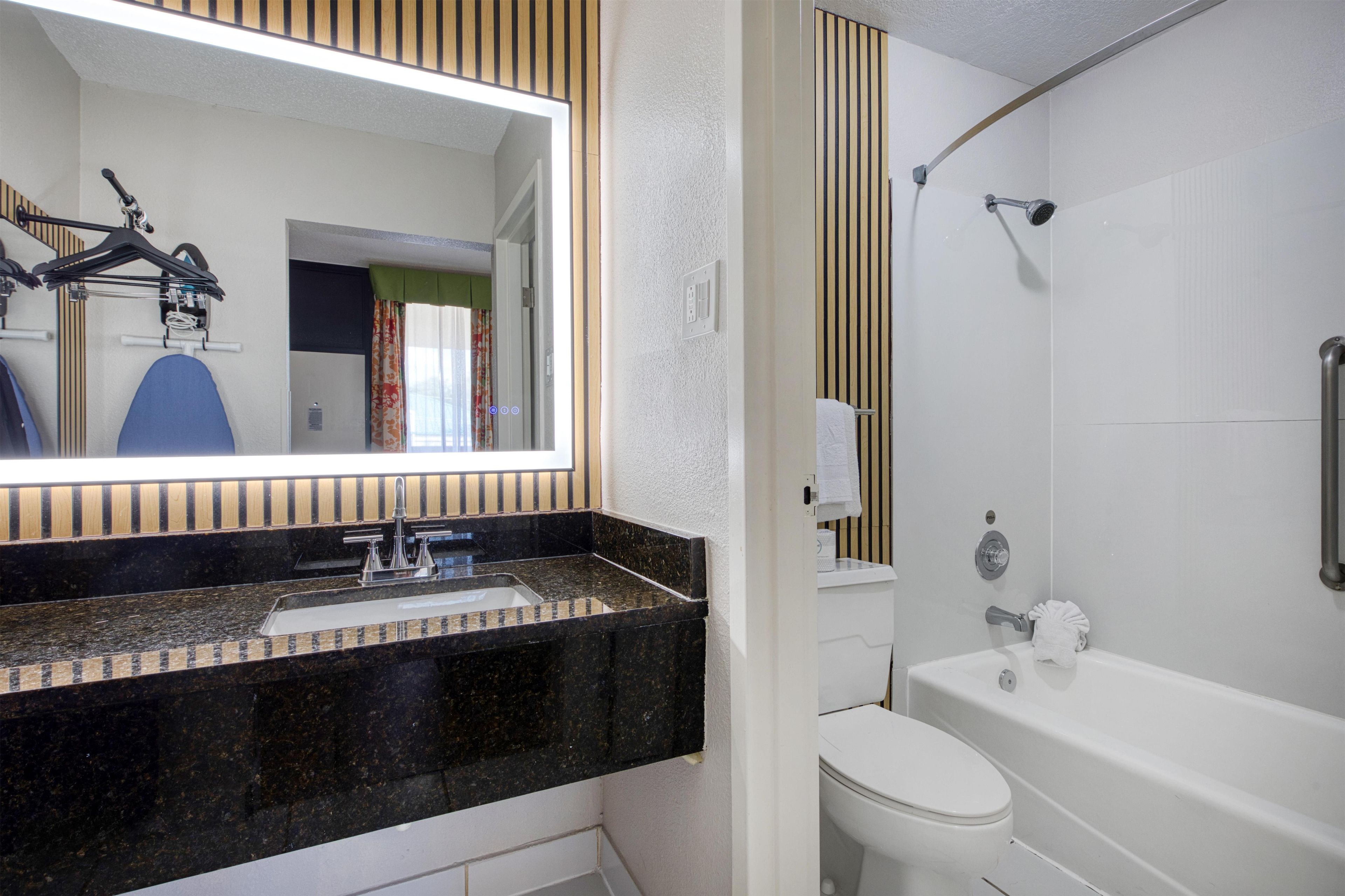 Un baño con encimera de granito negro, inodoro blanco, bañera y ducha.