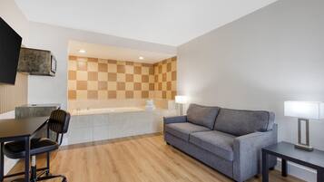 A modern hotel room with a checkered wall, a sofa, a desk with a chair, a lamp, and a flat-screen TV mounted on the wall.