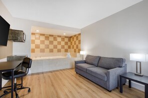 A modern hotel room with a checkered wall, a sofa, a desk with a chair, a lamp, and a flat-screen TV mounted on the wall. - Best Western Irving Grapevine DFW North (Irving)