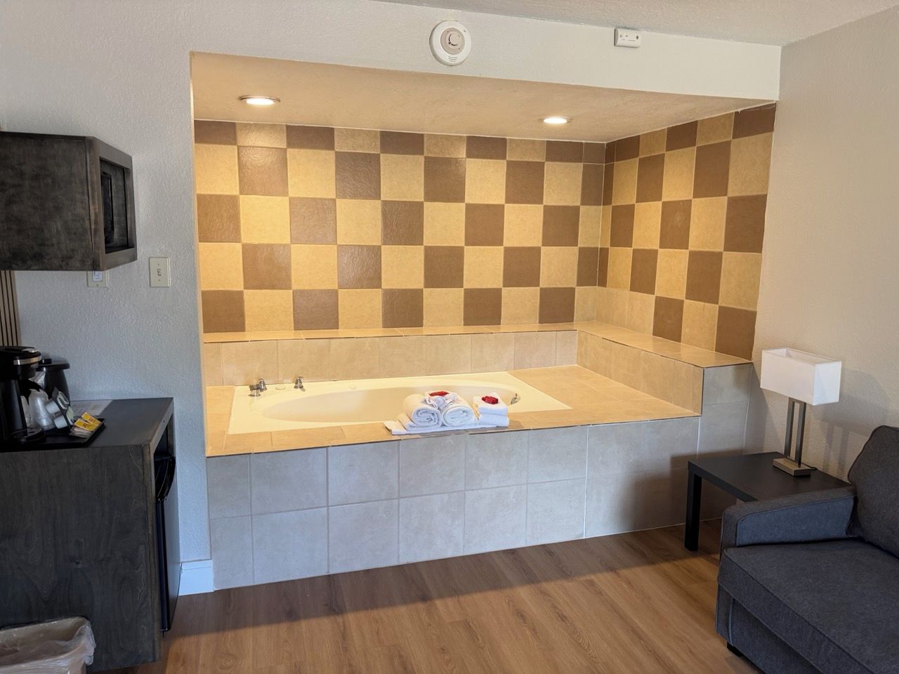 Ein modernes Badezimmer mit einer karierten Fliesenwand, einer integrierten Badewanne und einem kleinen Tisch mit einer Lampe.
