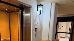 An elevator with a wooden interior, a wall-mounted emergency phone, and a sign indicating a fire exit.