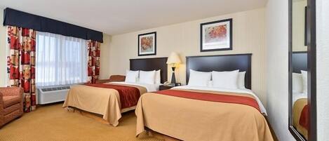 A hotel room with two beds, a sofa, a lamp, and a large mirror.