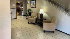 A hotel lobby with a reception desk, two armchairs, a table with a lamp, a potted plant, and a painting on the wall. - Quality Inn & Suites Farmington (Farmington)