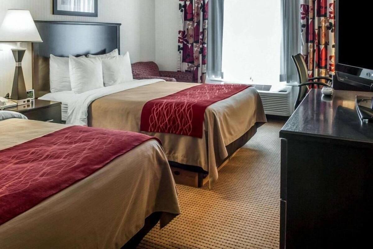 Une chambre d’hôtel avec deux lits, un bureau, une télévision et une fenêtre avec des rideaux.