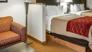 A hotel room with a bed, two bedside lamps, a patterned armchair, and artwork on the walls. - Quality Inn & Suites Farmington (Farmington)