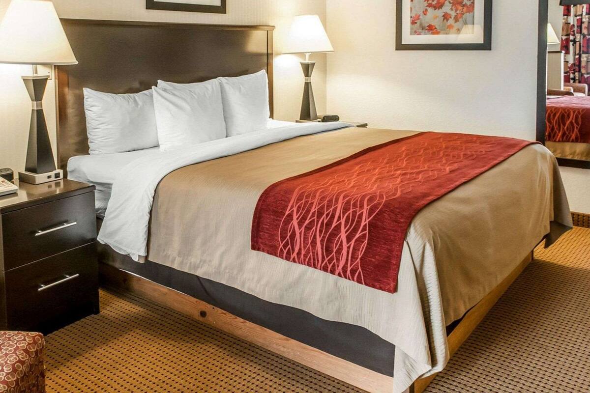 Une chambre d’hôtel avec un grand lit, deux tables de chevet, une petite table, une chaise et deux lampes fixées au mur.
