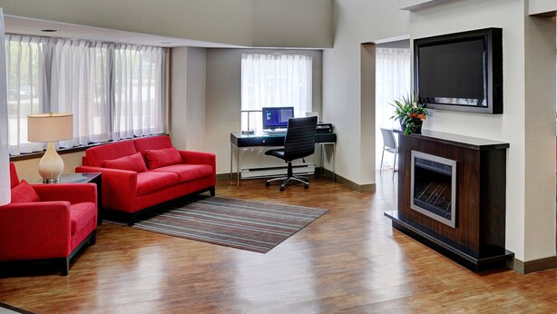 A spacious living room with a red sofa, a desk with a computer, a fireplace, and a TV mounted on the wall. - Comfort Inn Thunder Bay (Thunder Bay)