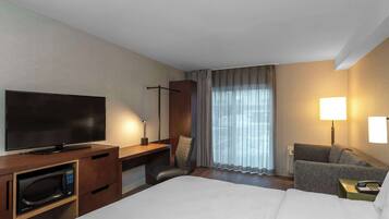 A hotel room with a bed, a TV, a desk with a chair, a microwave, a sofa, and a lamp.
