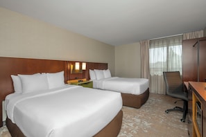 A hotel room with two beds, a desk, a chair, and a window with curtains.