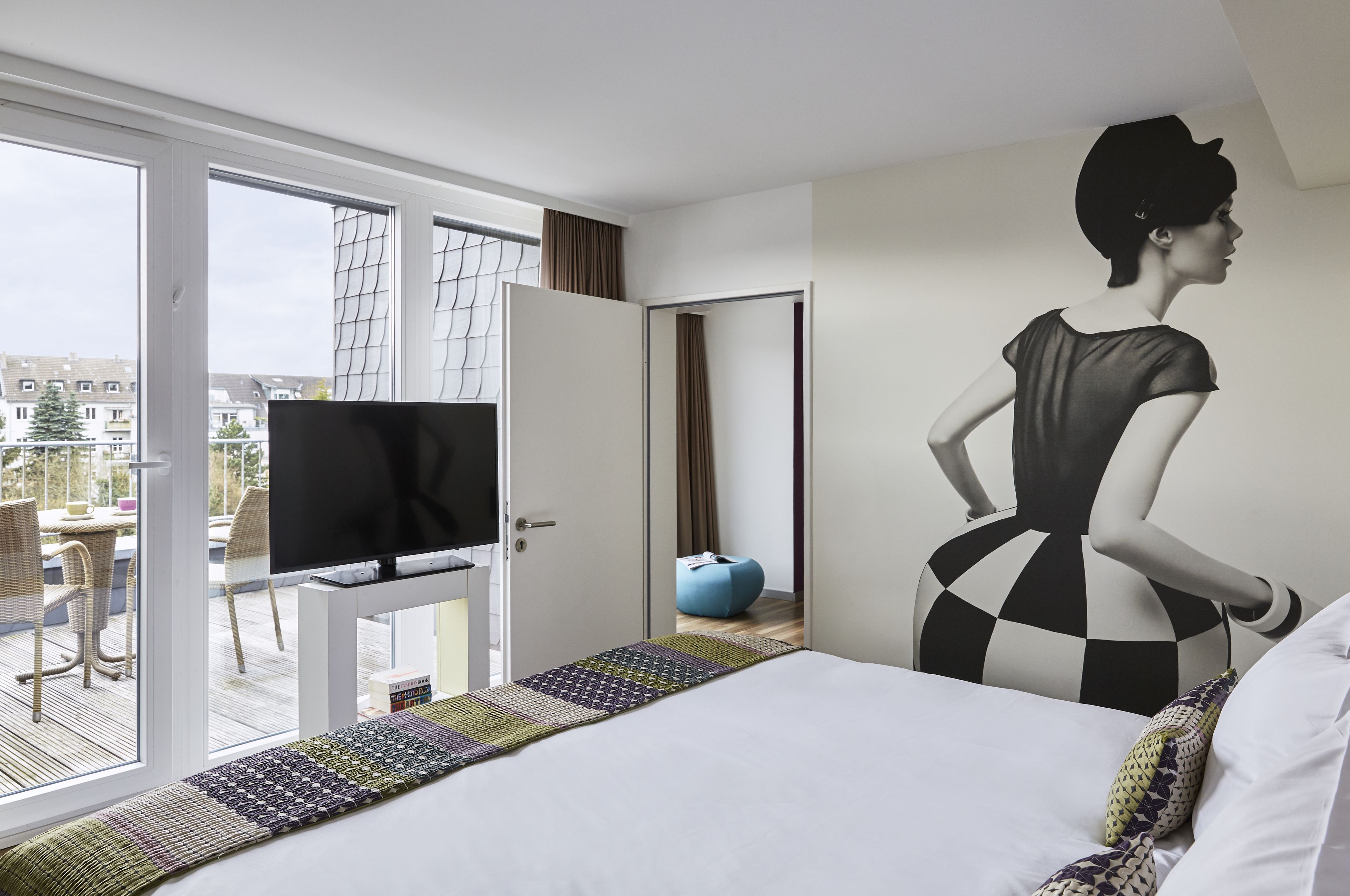 A hotel room with a bed, a television, a large window, and a view of the outside.