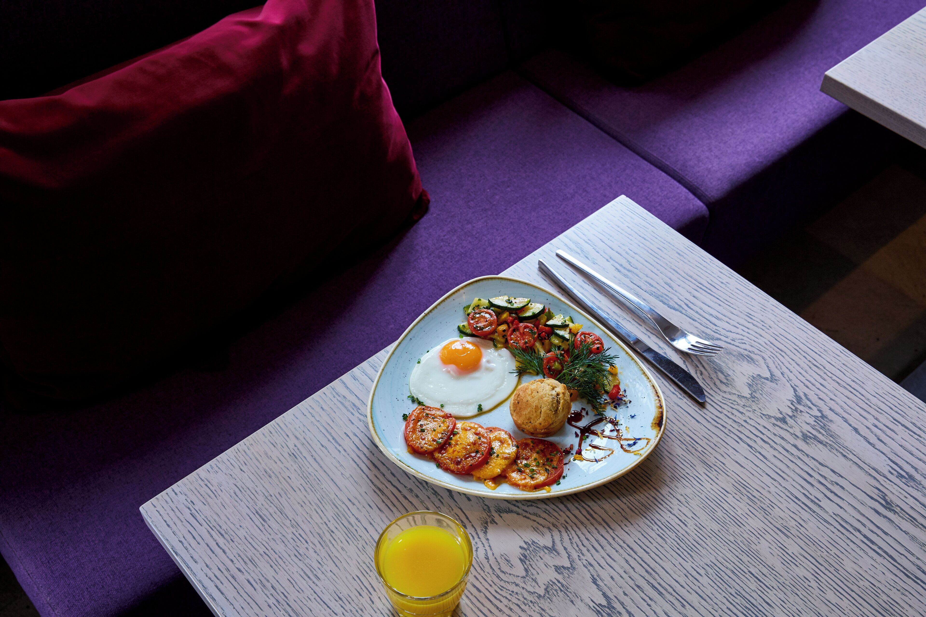 A dining table with a plate of food, a glass of juice, and cutlery.