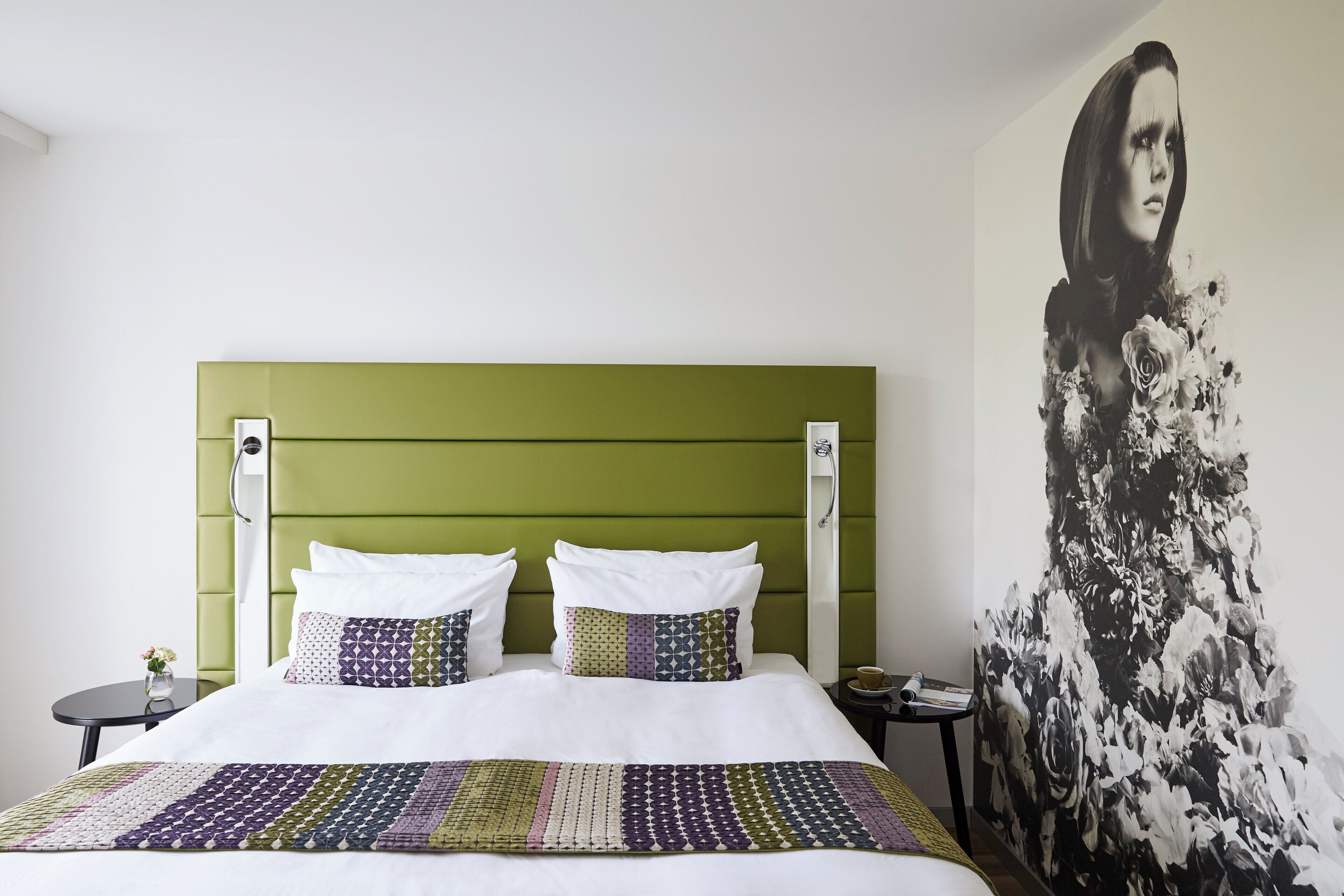Una cama con cabecera verde, ropa de cama blanca y una manta estampada.