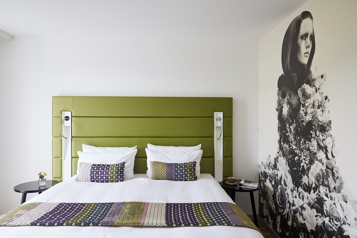 Een bed met een groen hoofdeinde, wit beddengoed en een bedsprei met een patroon.