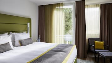 A hotel room with a large bed, a chair, and a view of greenery outside.