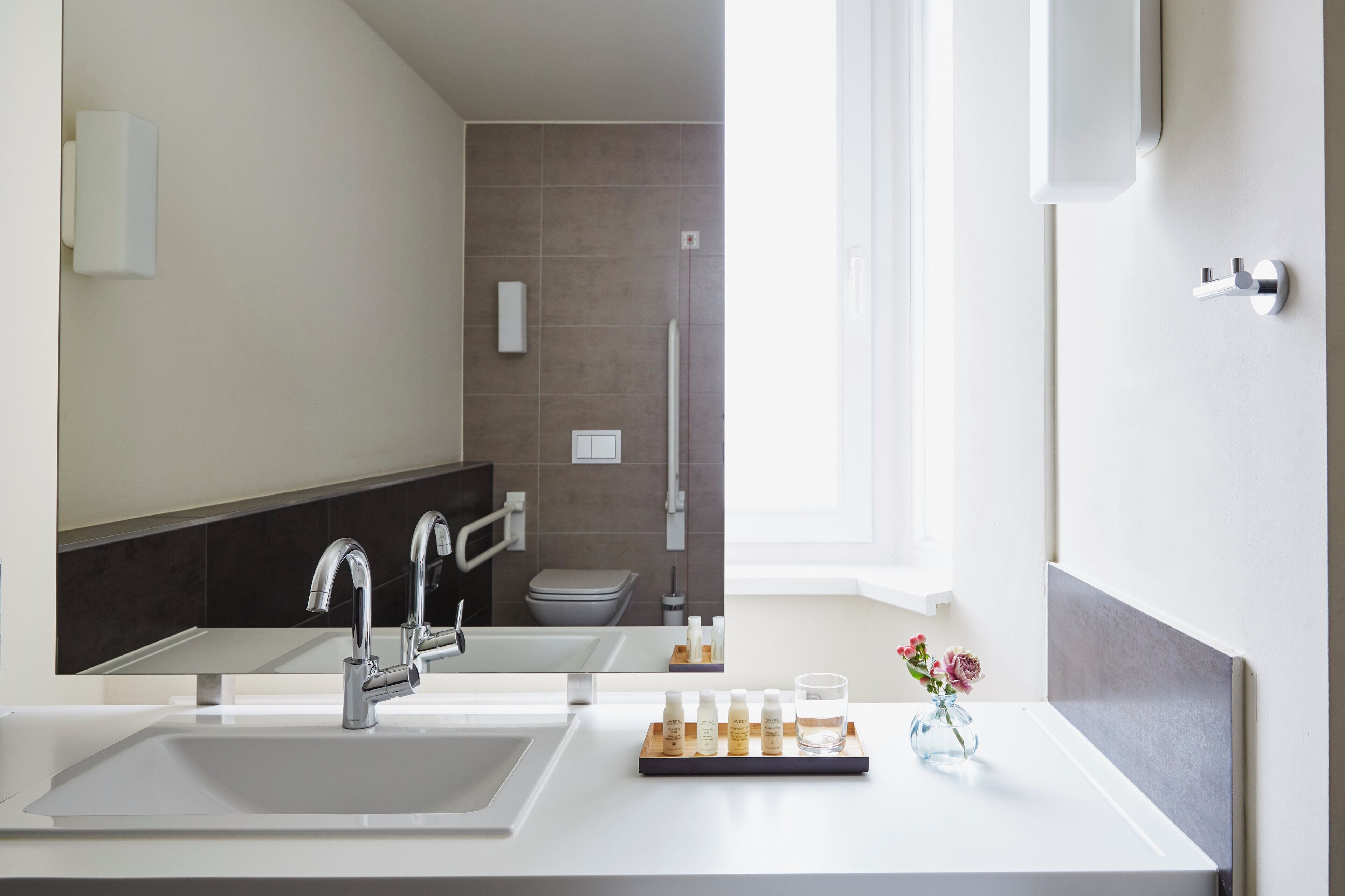Ein modernes Badezimmer mit großem Spiegel, zwei Waschbecken, einer Dusche und einem Fenster.