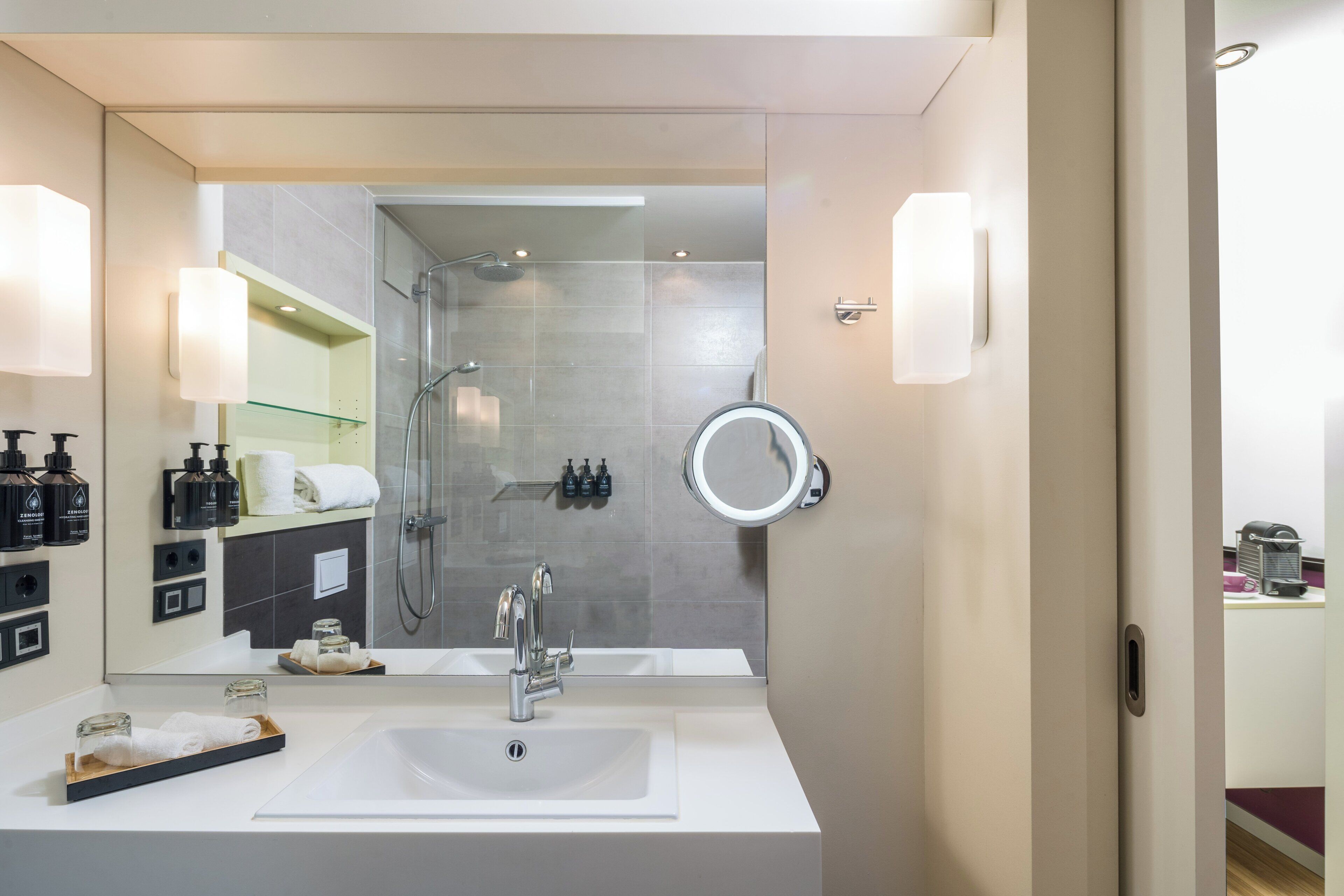 Une salle de bain moderne avec un grand miroir, un lavabo et un espace douche.